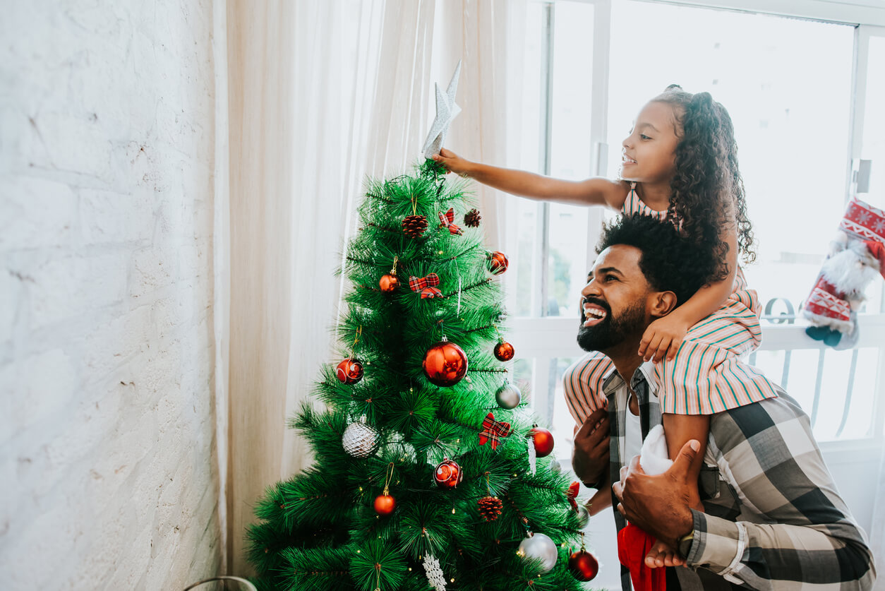 pai com criança decorando árvore de natal