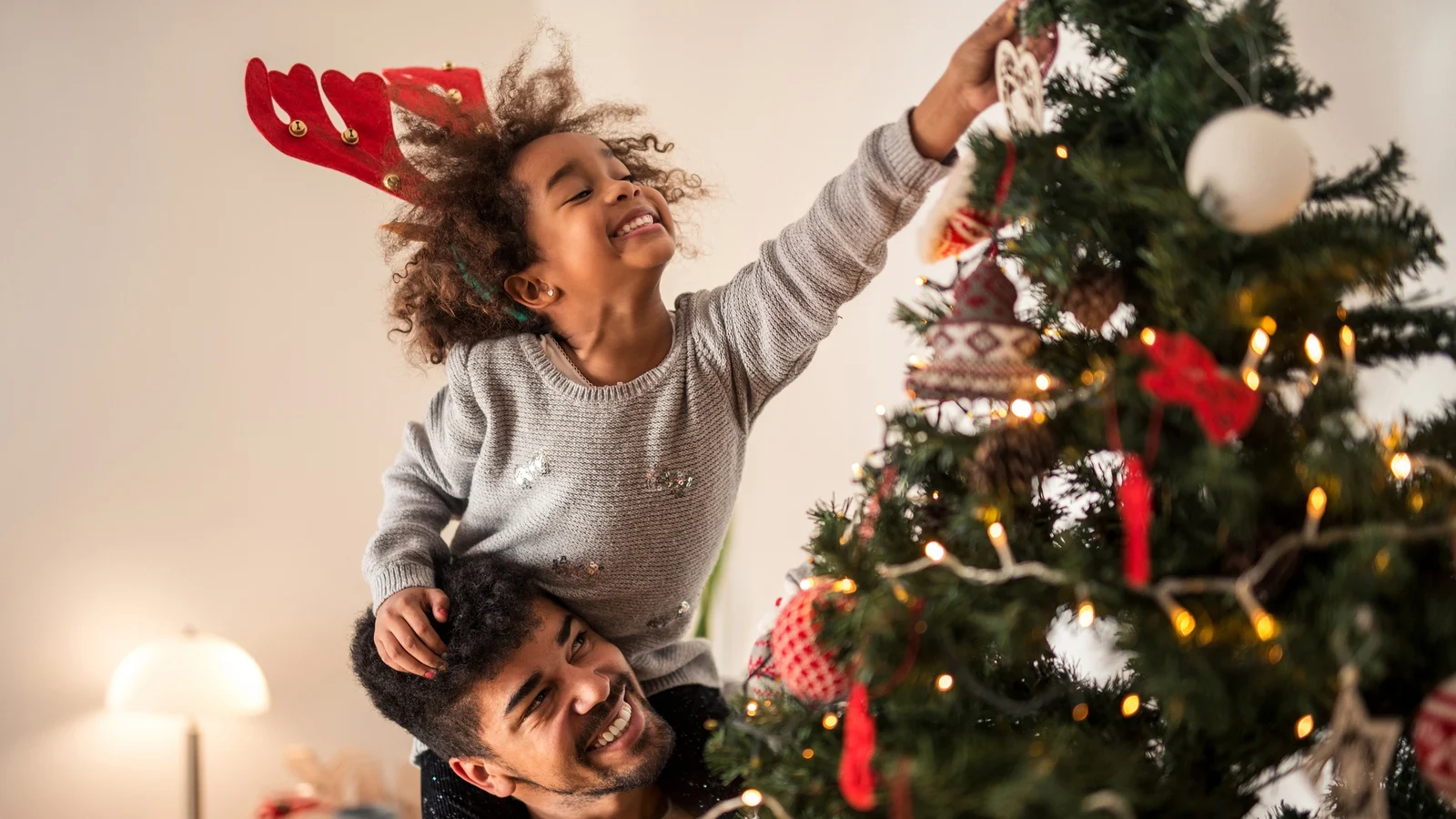 criança pendurando enfeite em árvore de natal