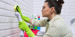 mulher limpando parede de azulejos em banheiro