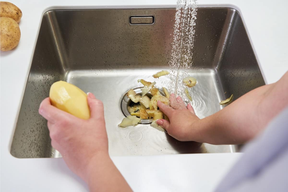 pessoa colocando cascas de batata em triturador de lixo da pia da cozinha