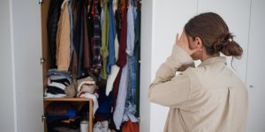 mulher olhando preocupada para guarda-roupa cheio e bagunçado